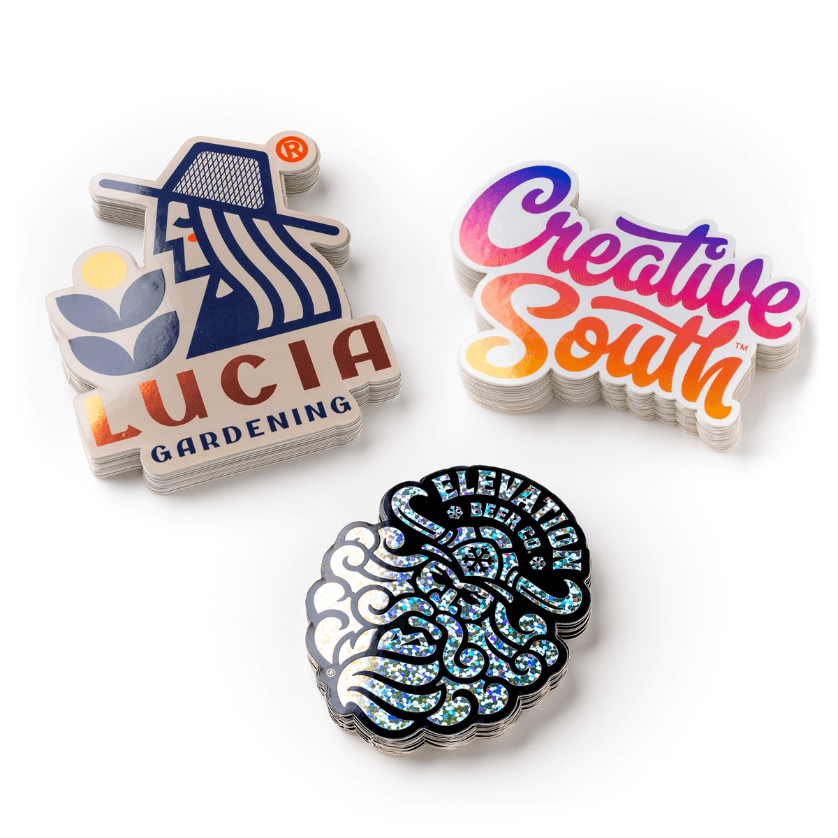 Three colorful stickers: one with "LUCIA GARDENING" and a figure, another with "Creative South," and a third with a shiny intricate design.