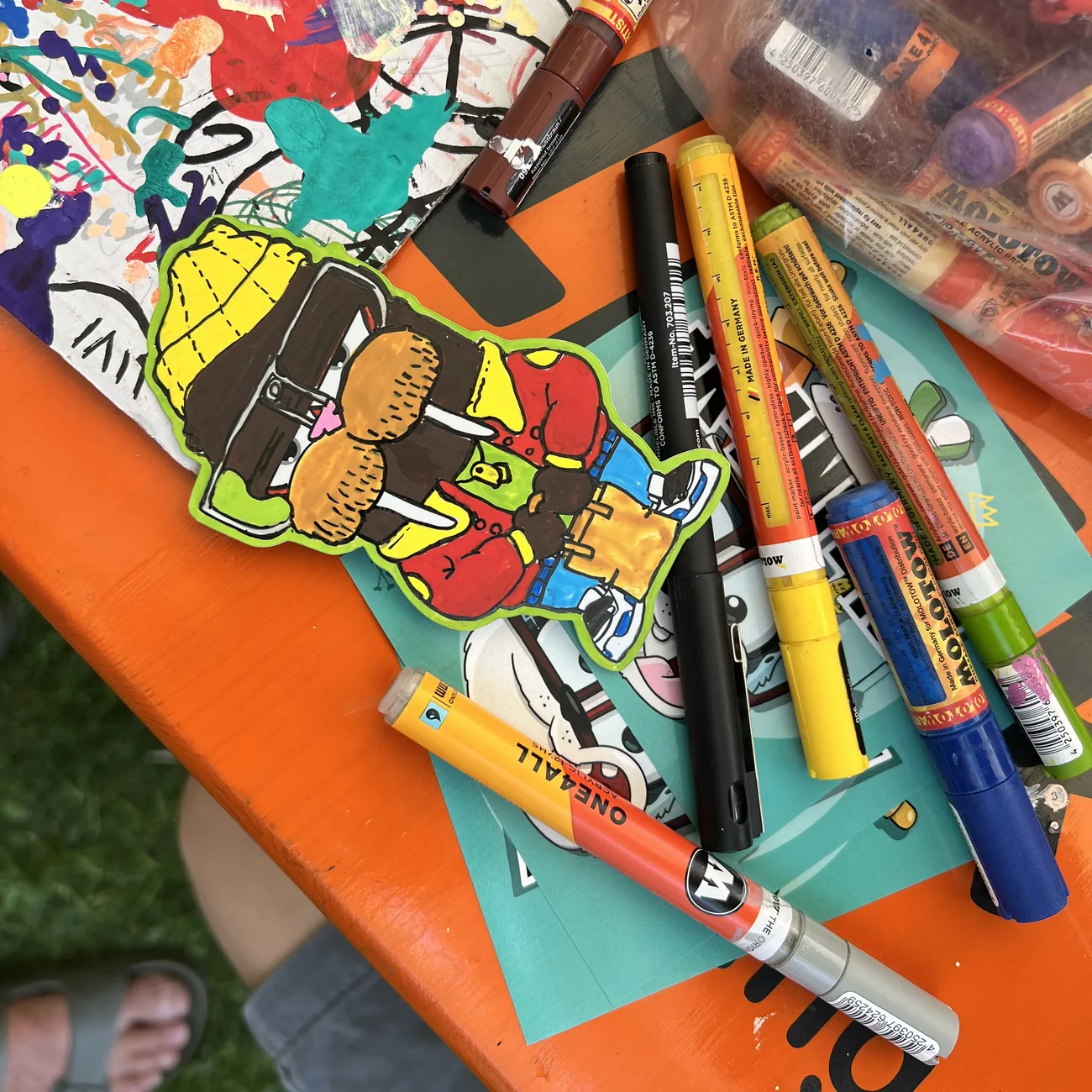Hand-colored Brainfart die-cut sticker of a character in a yellow beanie and red jacket, surrounded by paint markers