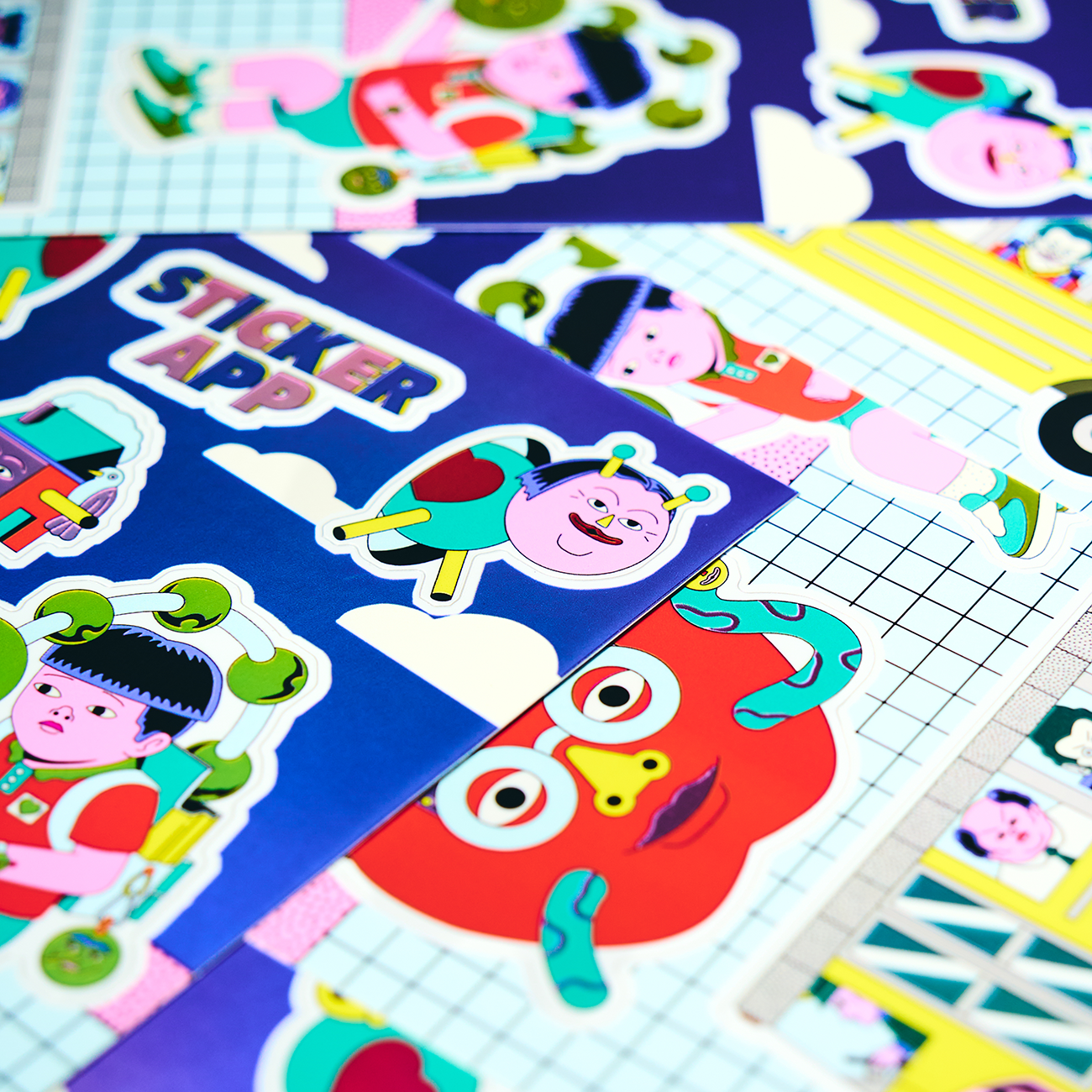 colorful sticker sheets laying scattered on a table, with an apple, cartoon insects, and the test "STICKERAPP".