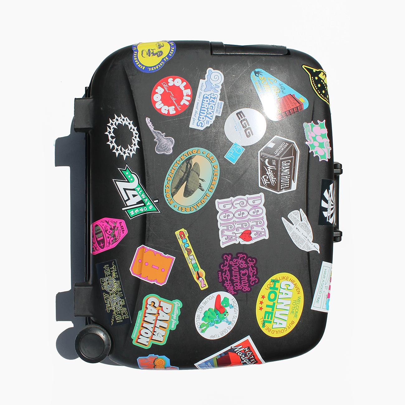 black suitcase covered in colorful die-cut stickers in different shapes, against a white background