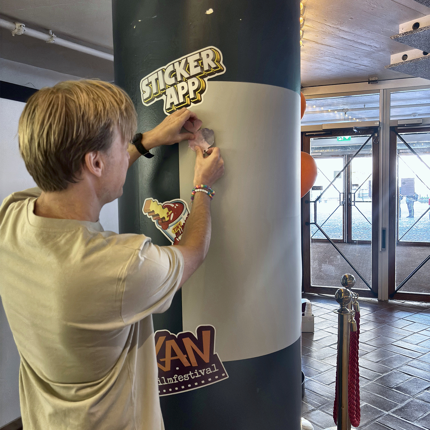Man placing a sticker on a StickerApp sticker wall wrapped around a pillar at KAN filmfestival
