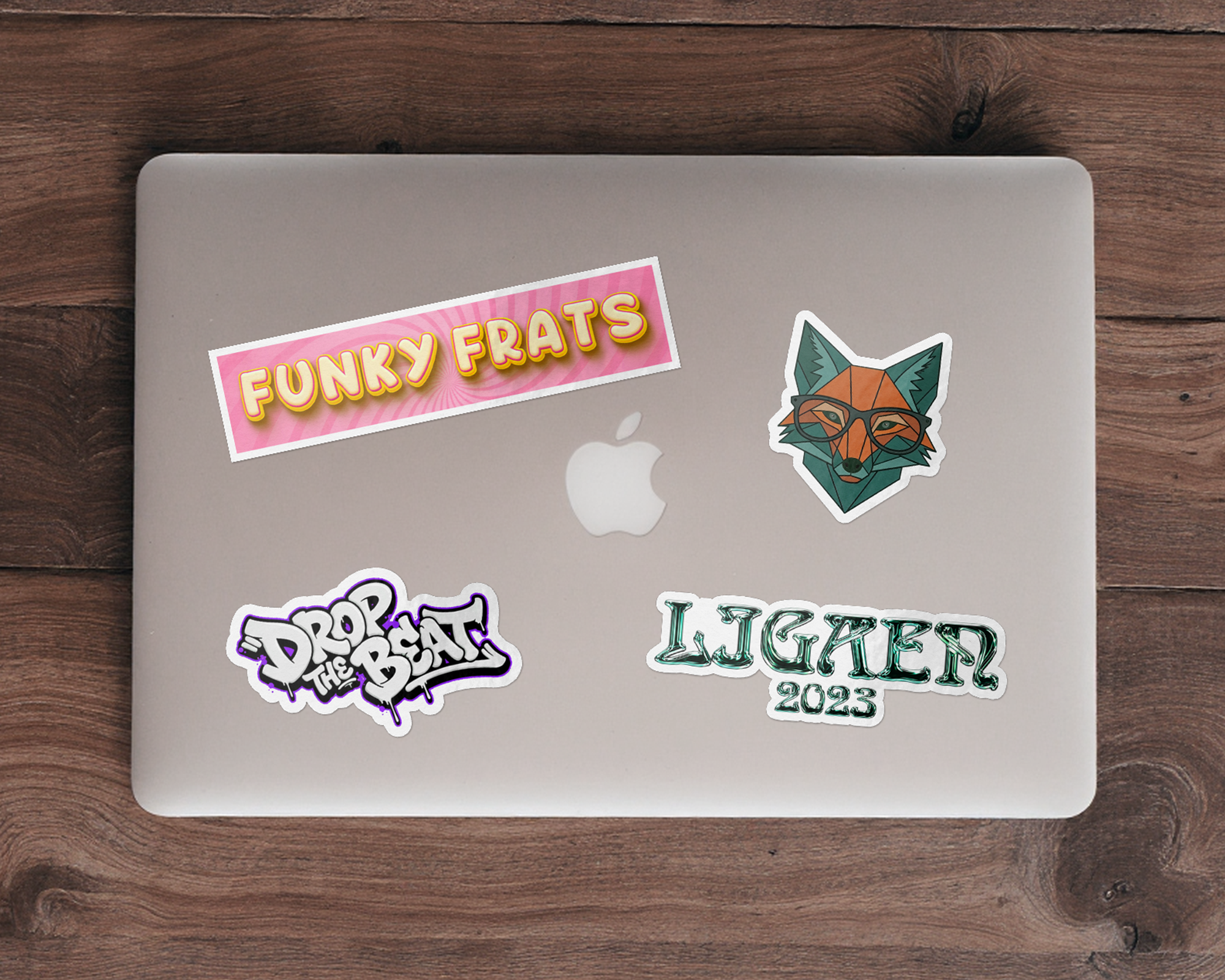 Silver laptop on a wooden table with four die-cut laptop stickers, including a fox in glasses