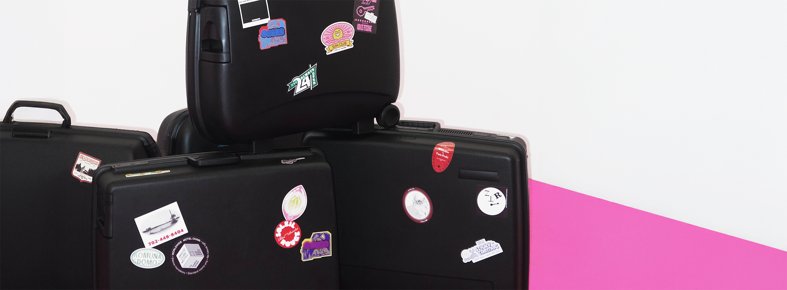 various black suitcases decorated with die-cut stickers, against a pink and white background