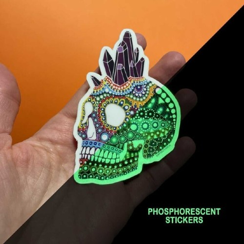 Hand holding a mandala skull sticker by mpgautheron, half shown glowing green in the dark